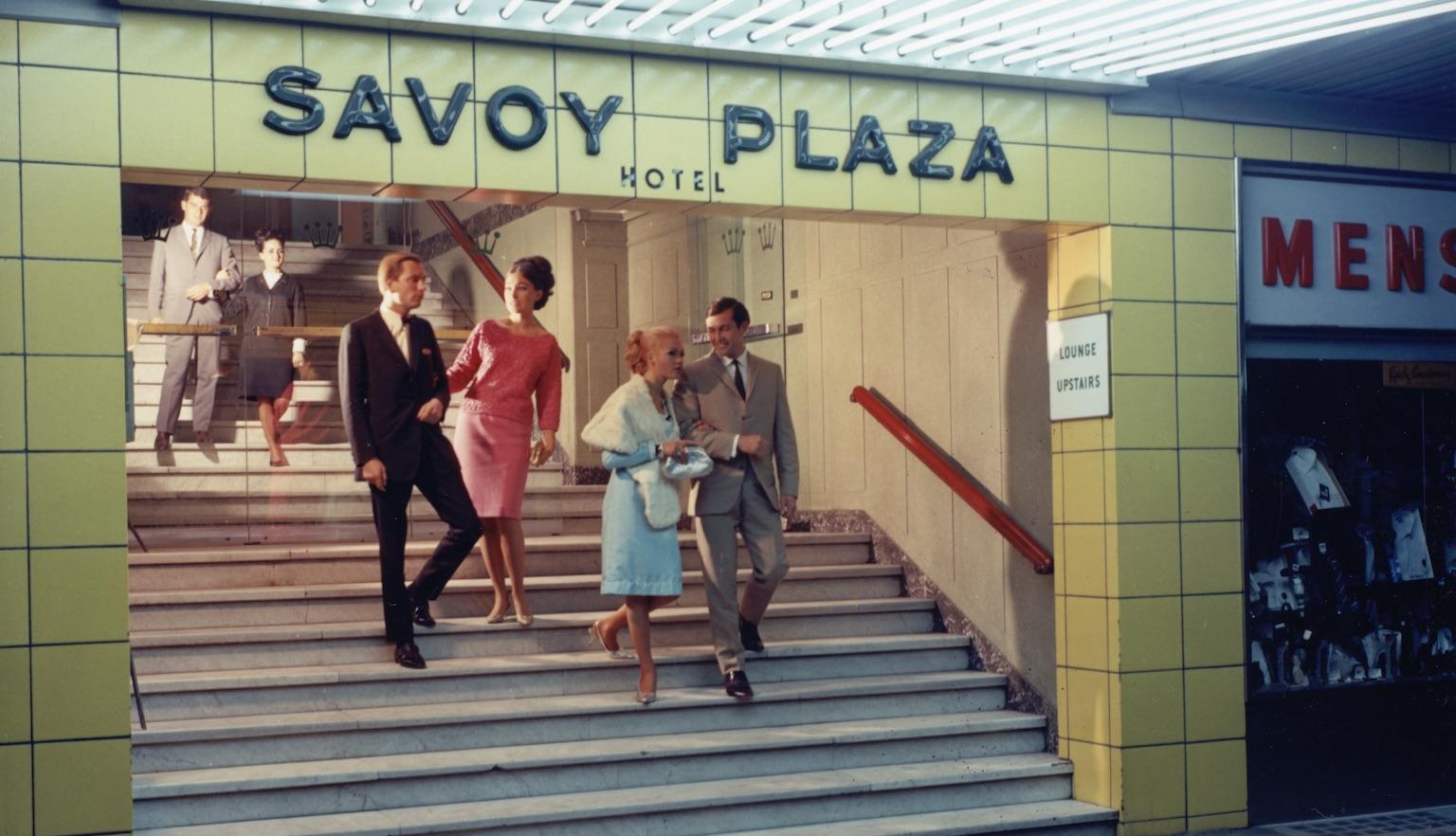 Three well-dressed couples leaving the Savoy Plaza Hotel and walking towards the street where a shiny car is parked