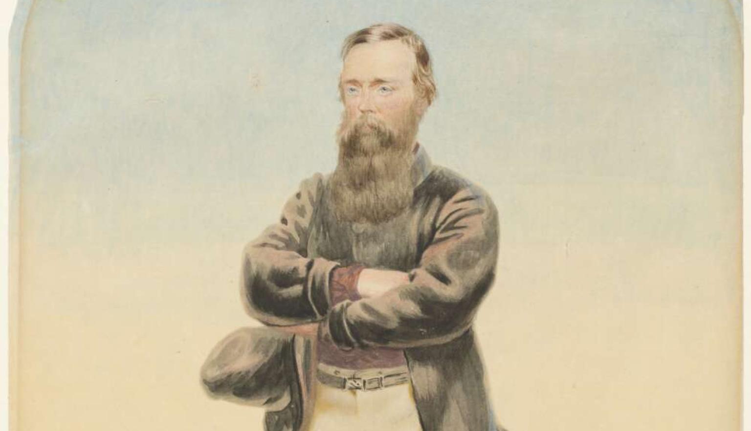 A man standing arms folded in a strong pose standing in front of a saddle and camel