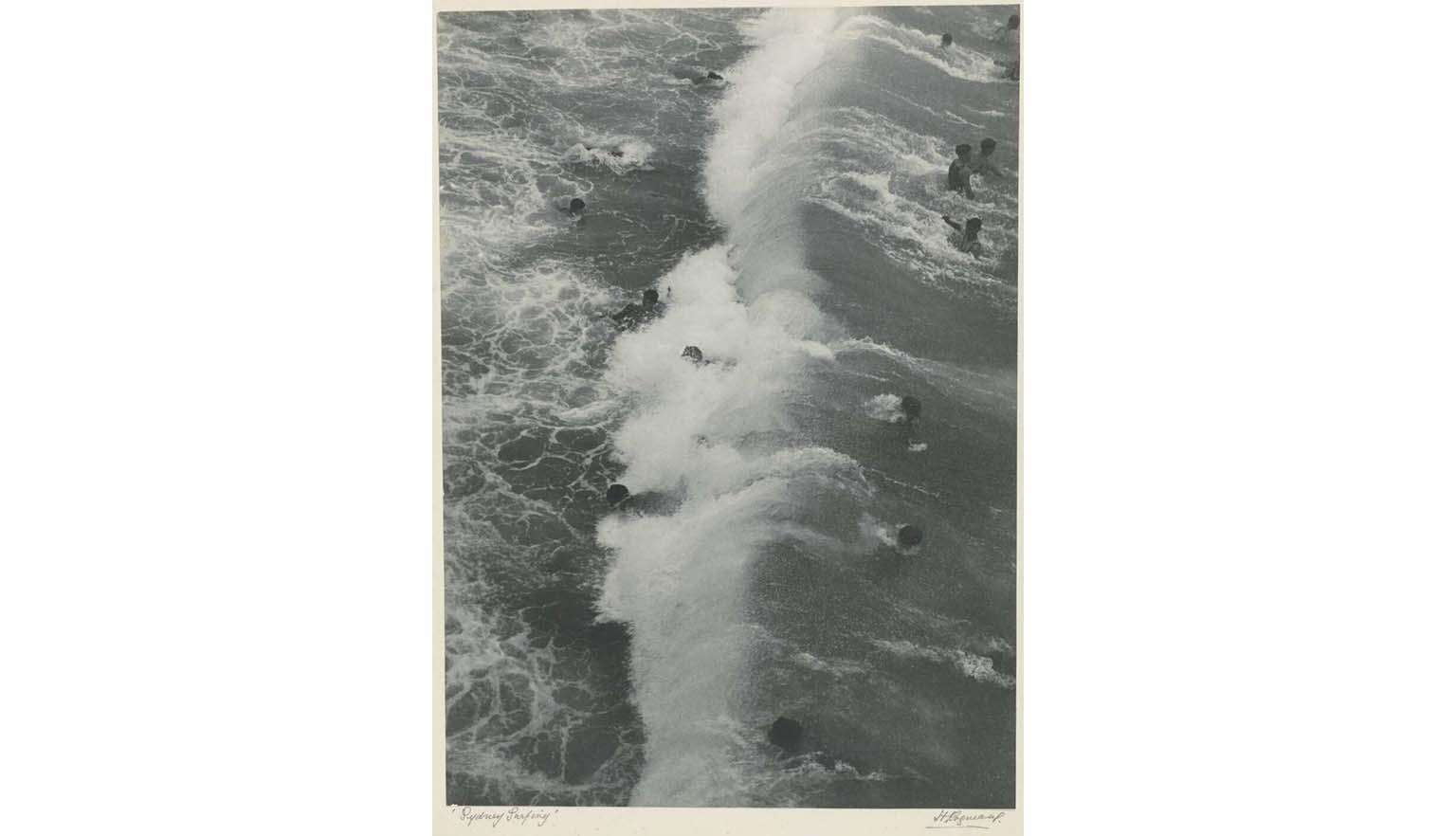 Black and white photo of people swimming in the surf. 'Sydney surfing' is handwritten on the bottom left and 'H Cazneeaux' on the bottom right collection-photo-sydney-surfing-cazneaux-1929-nla-obj-140180873-carousel