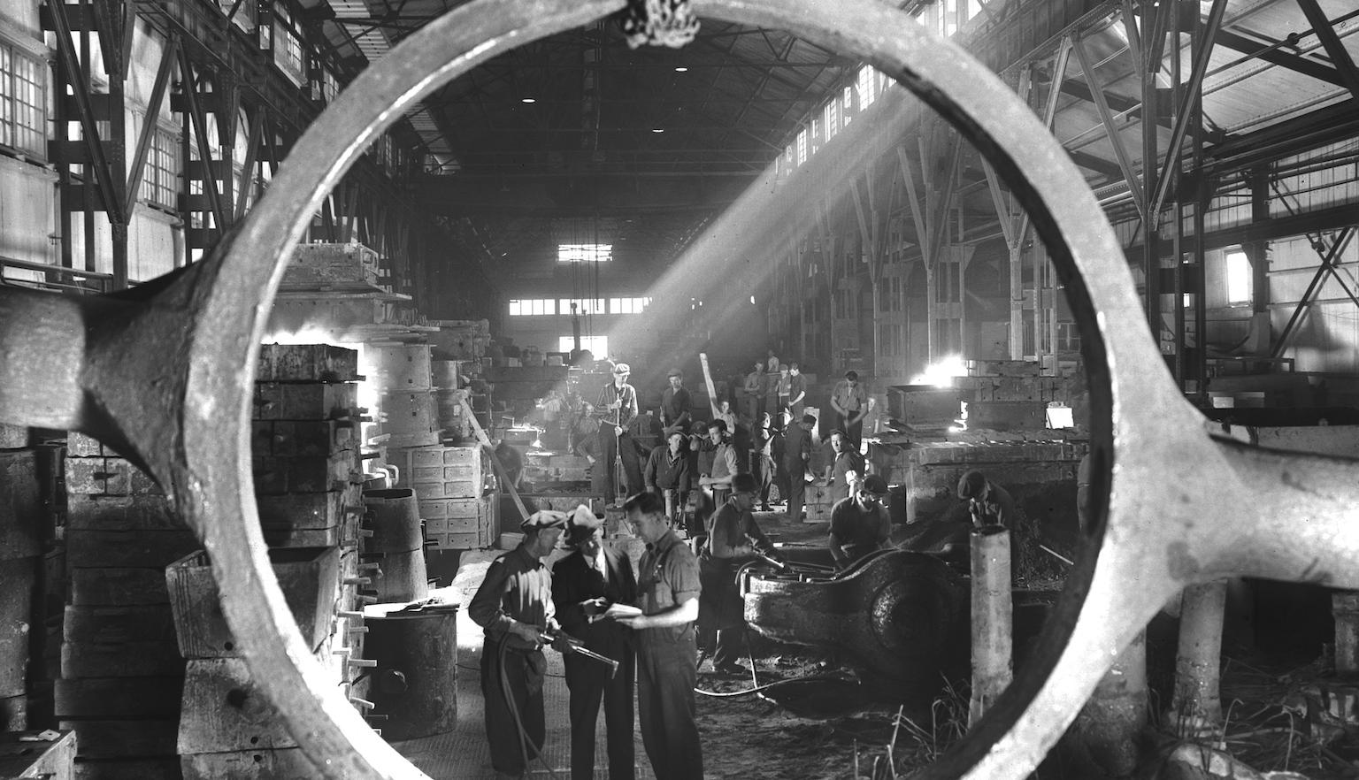 Photograph of employees at BHP steelworks viewed through a cast steel tilting frame of a slag post.