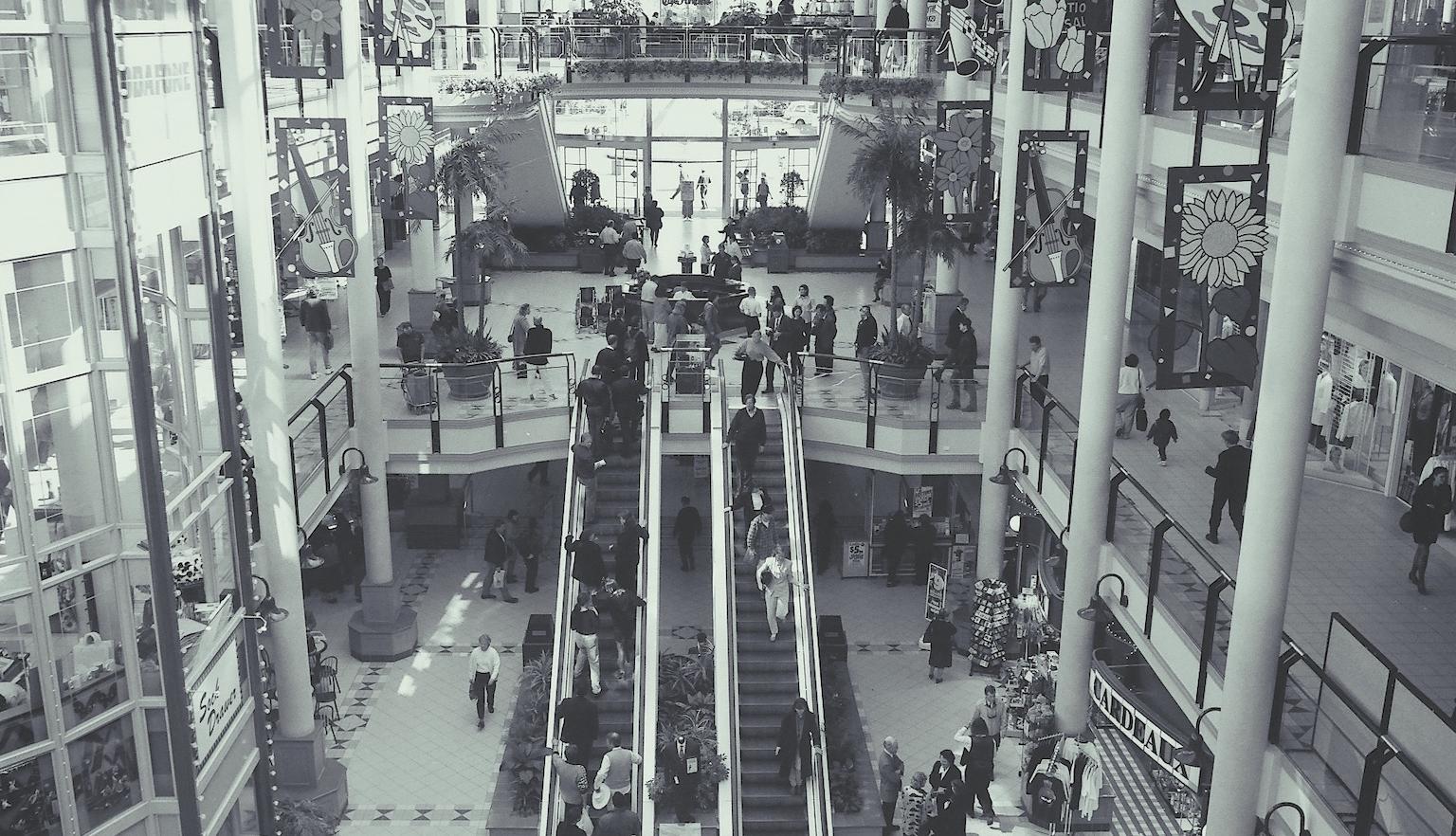 Black and white photo of a busy shopping centre where multiple floors of shops are visible