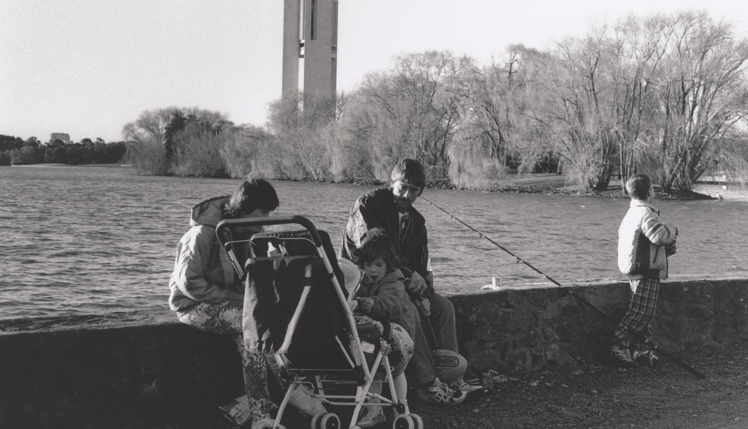 Black and white photo of a family with a stroller sitting at the edge of Lake Burley Griffin