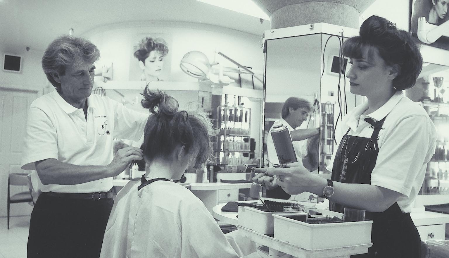 Black and white photo of two hairdressers working on a client's hair