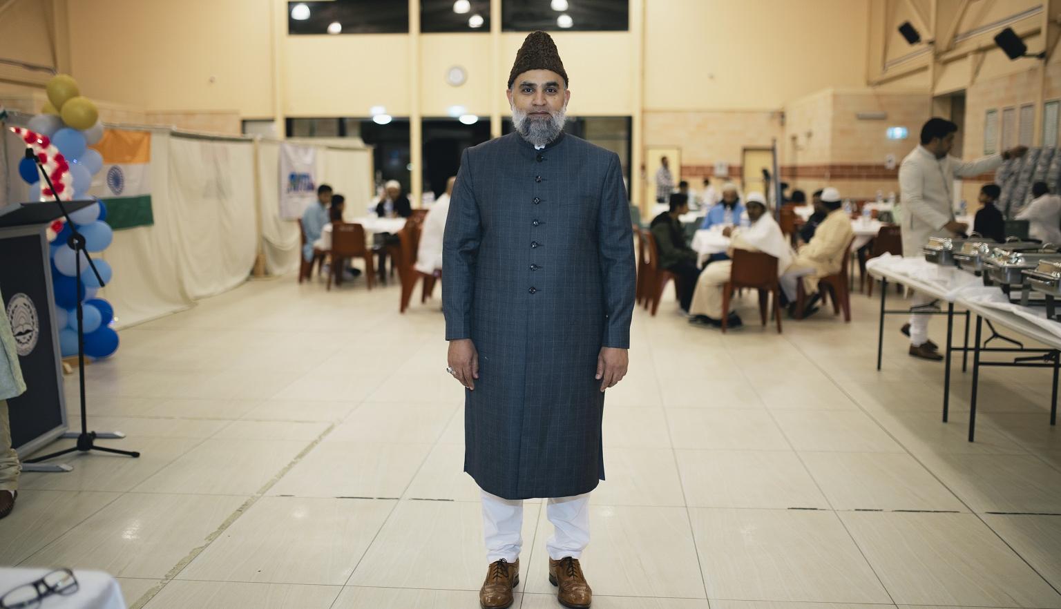 Man in cultural dress standing in front of tables set up for Eid Milap Dinner