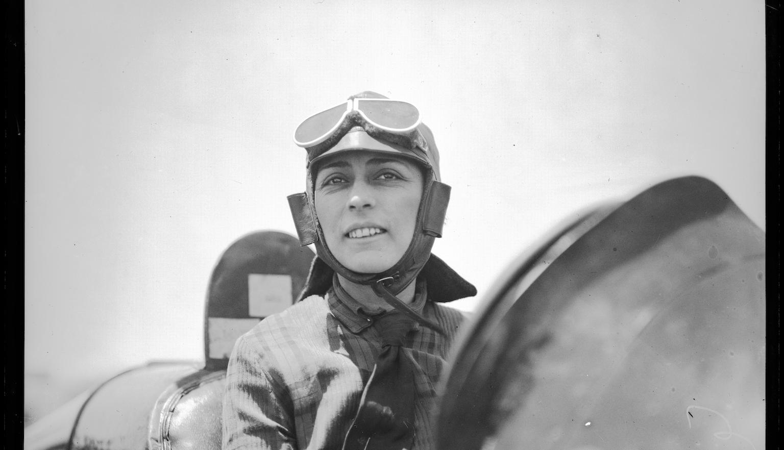 Black and white photo of a woman in goggles and a helmet sitting in a car