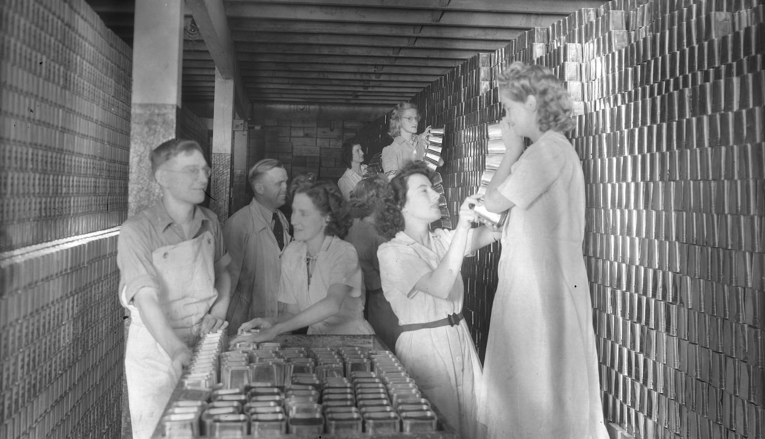 Workers packing tins of meat onto a trolley.