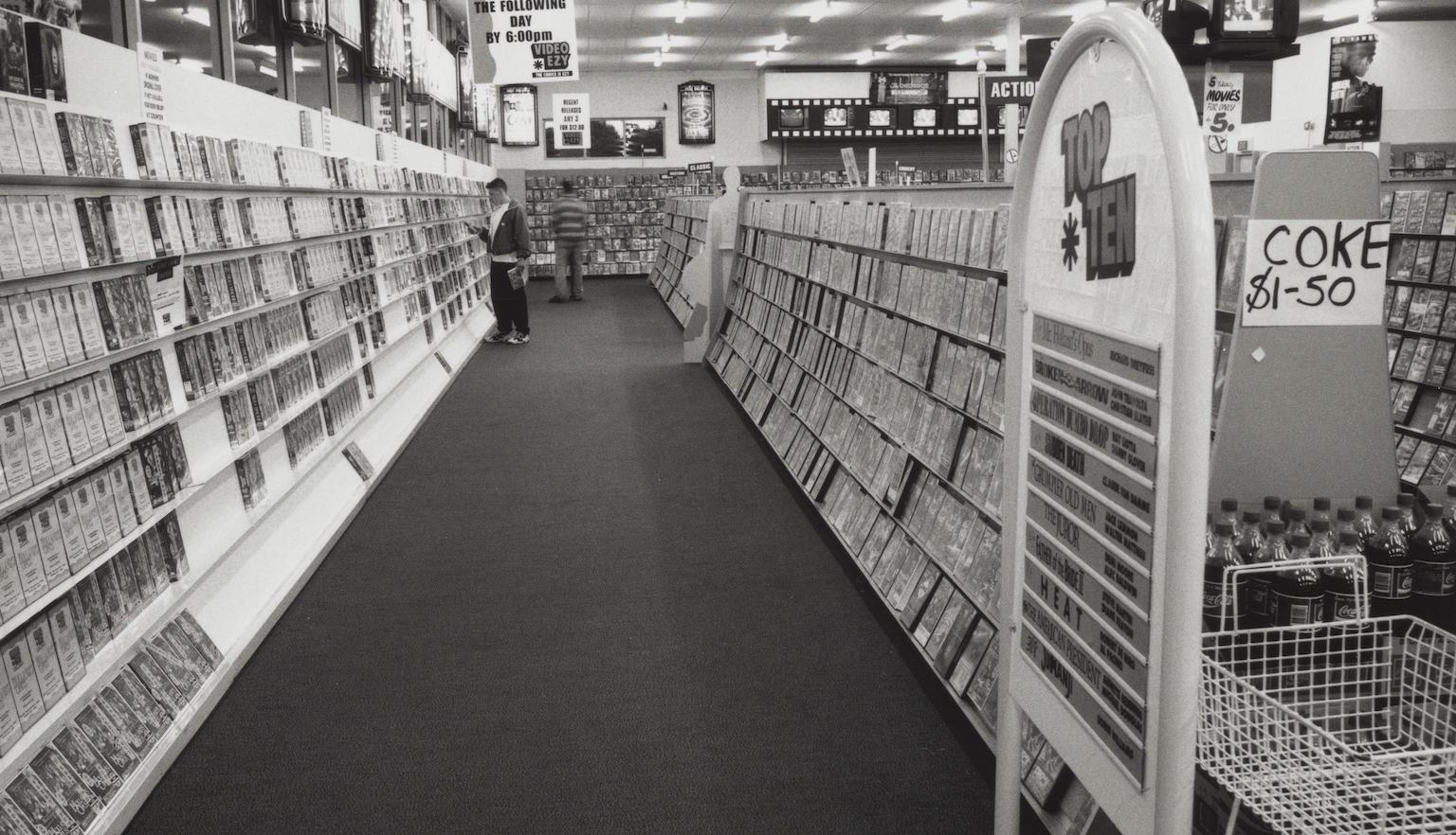 Black and white photo of an aisle in a video rental store