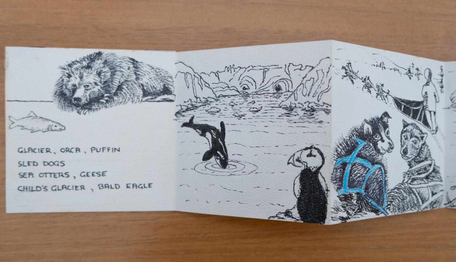Fold-out travel diary open to four pages with black and white illustrations of a bear, killer whale, puffin and sled dogs