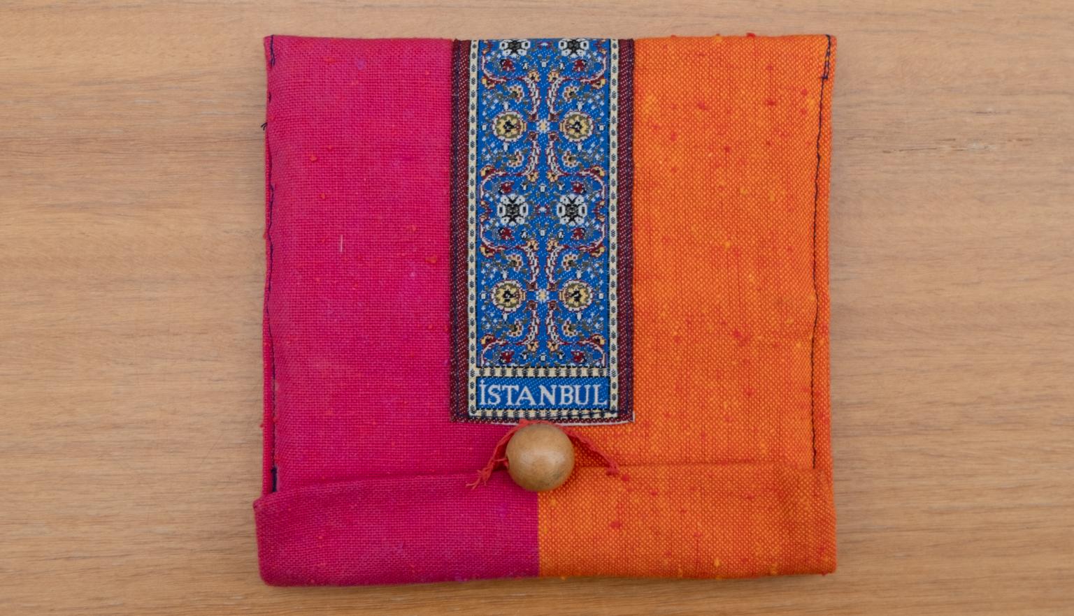 Pink, orange and dark blue slipcase, held closed with a round wooden bead, with small text reading 'Istanbul'