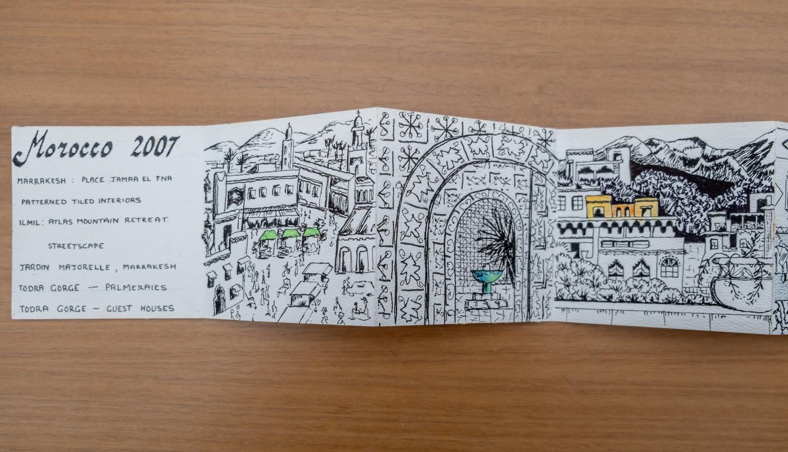 Fold-out travel diary open to three pages with black and white illustrations of Morocco streets and architecture