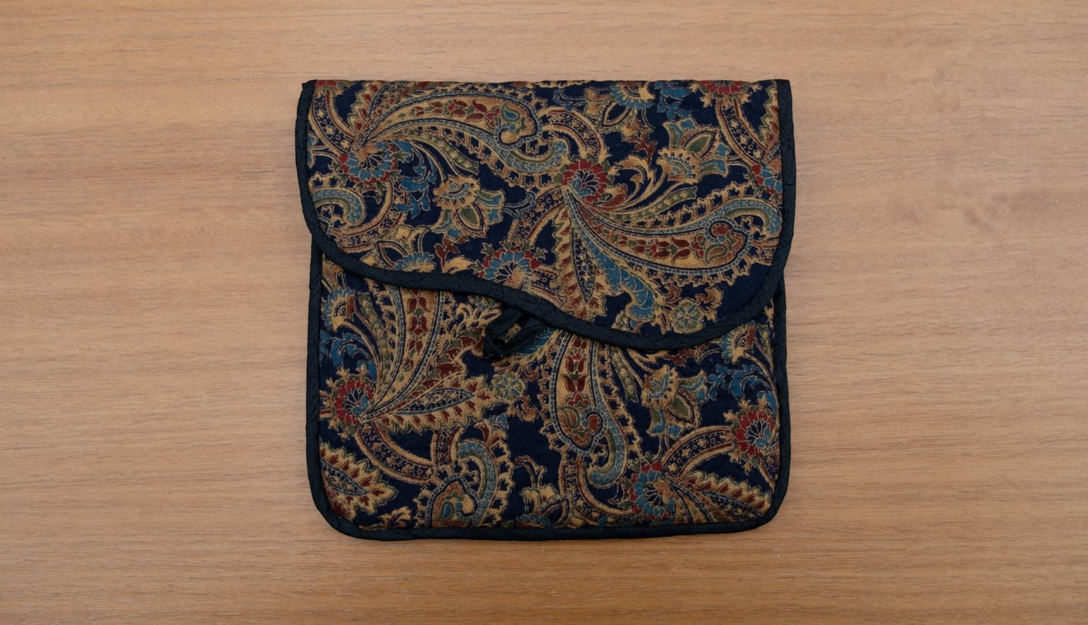 Fabric slipcase made of dark material with a paisley-like pattern in gold and dark jewel-tones