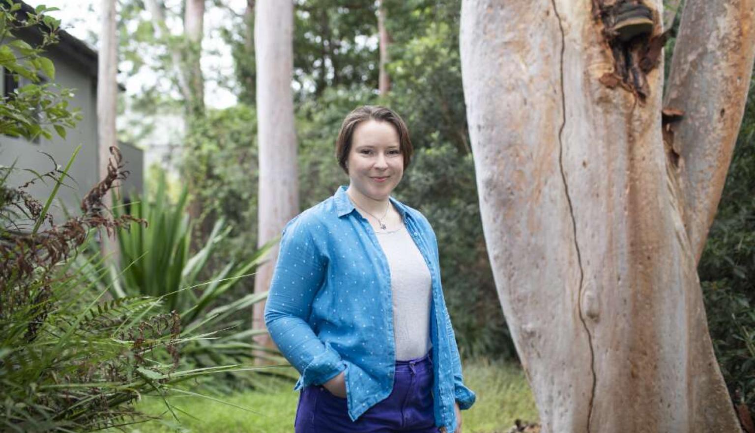 A woman in a blue shirt standing in front of a gum tree. 