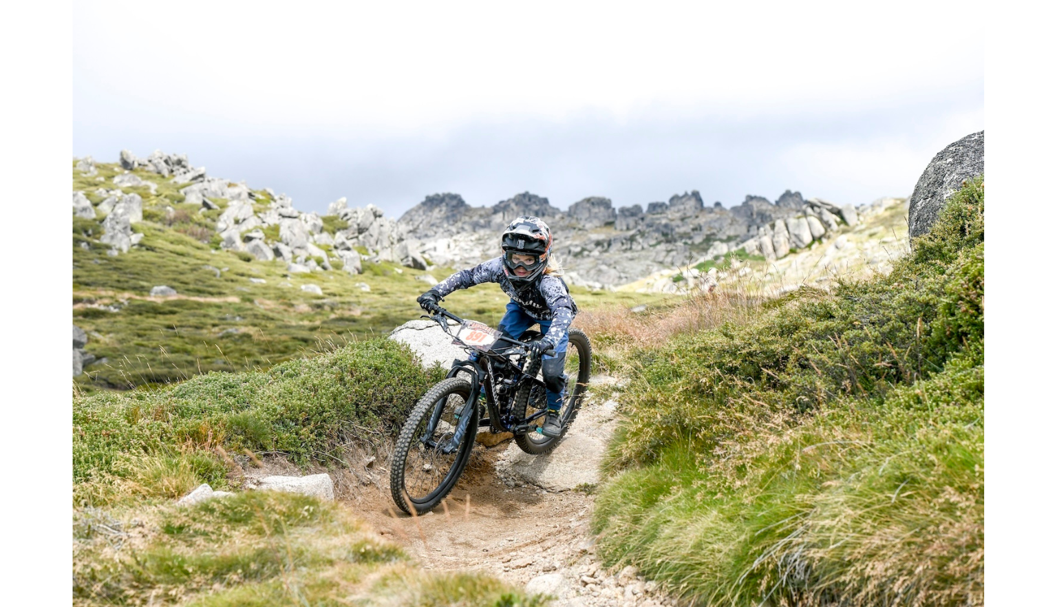 Mountain biker in full gear riding a rocky, dirt path on a cloudy day