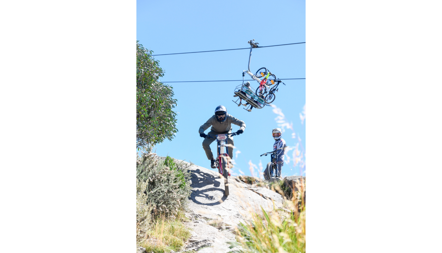 Mountain biker riding down a steep rocky path while another rider stands nearby