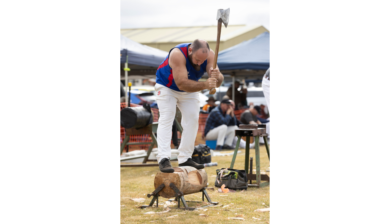 Man standing on a block of wood held up slightly above the ground and swinging an axe up to chop it in half