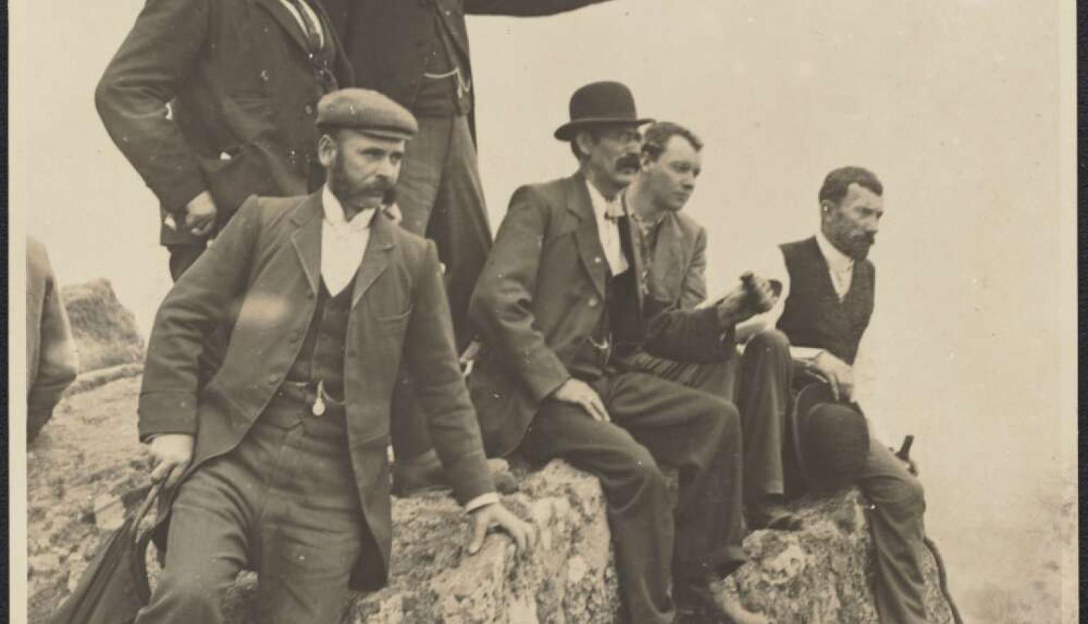 A black and wihte photo of a group of men sitting on a rock and looking over a field