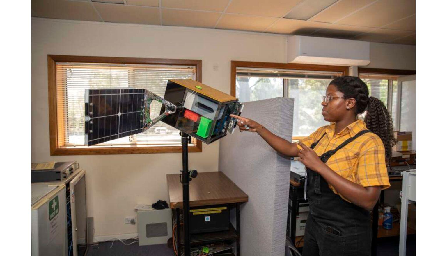  A photograph of a woman pointing a model of a satellite.