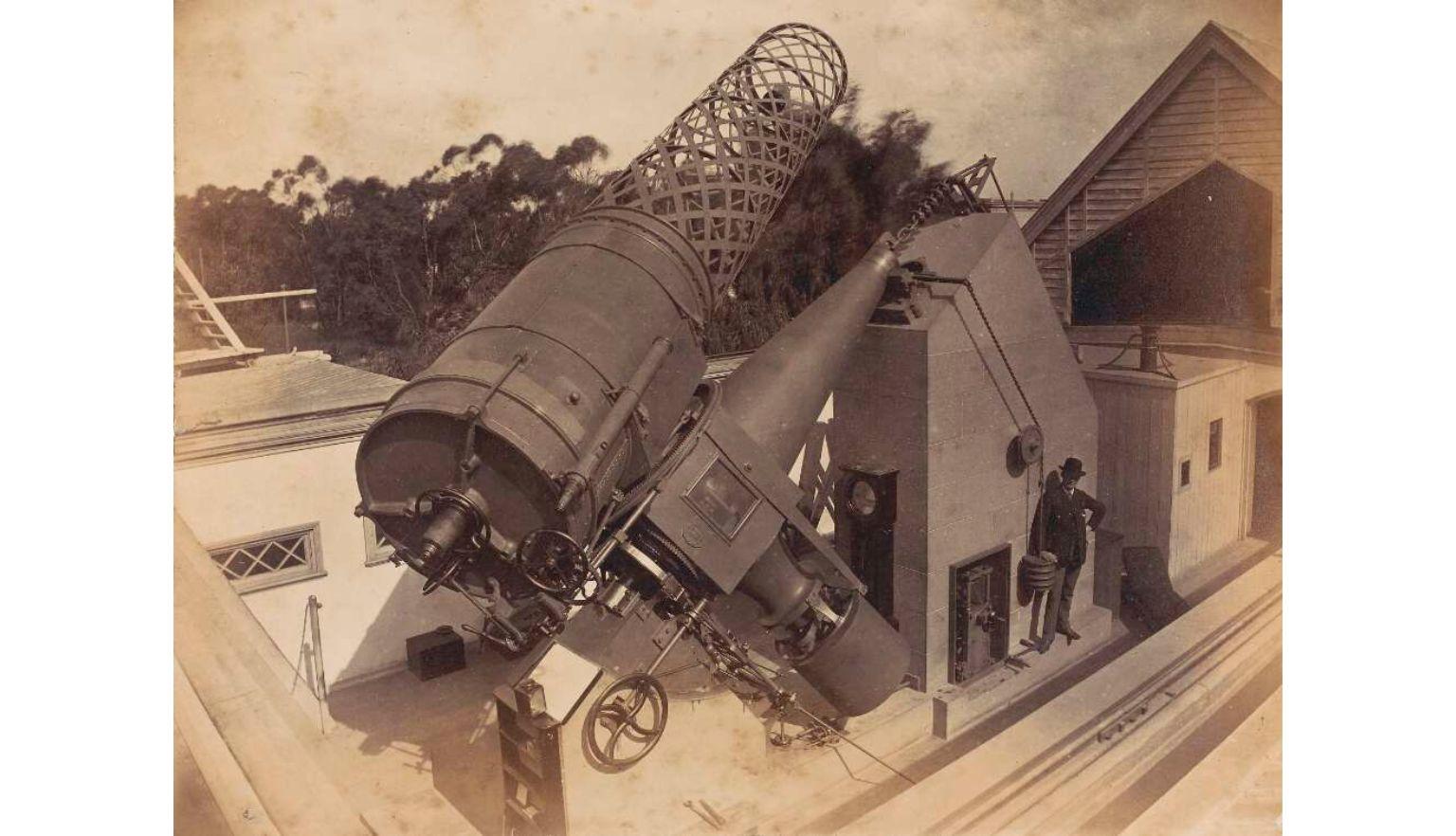 A yellowed photograph of a large optical telescope with a man standing beside it. 