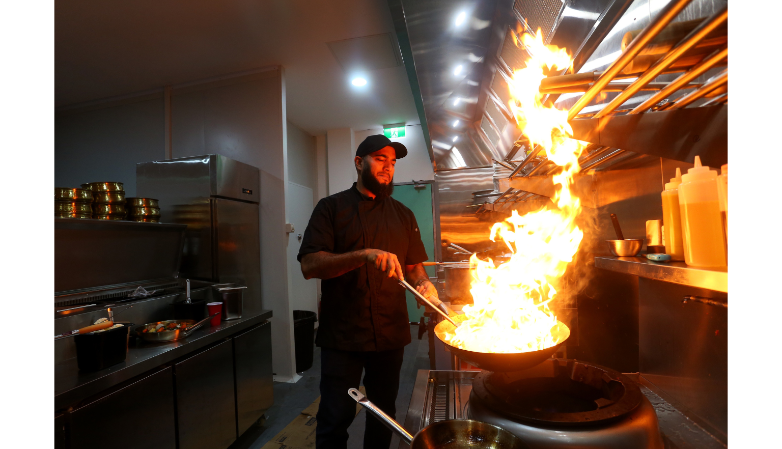 Man holding a pan with flames coming off it in an industrial kitchen