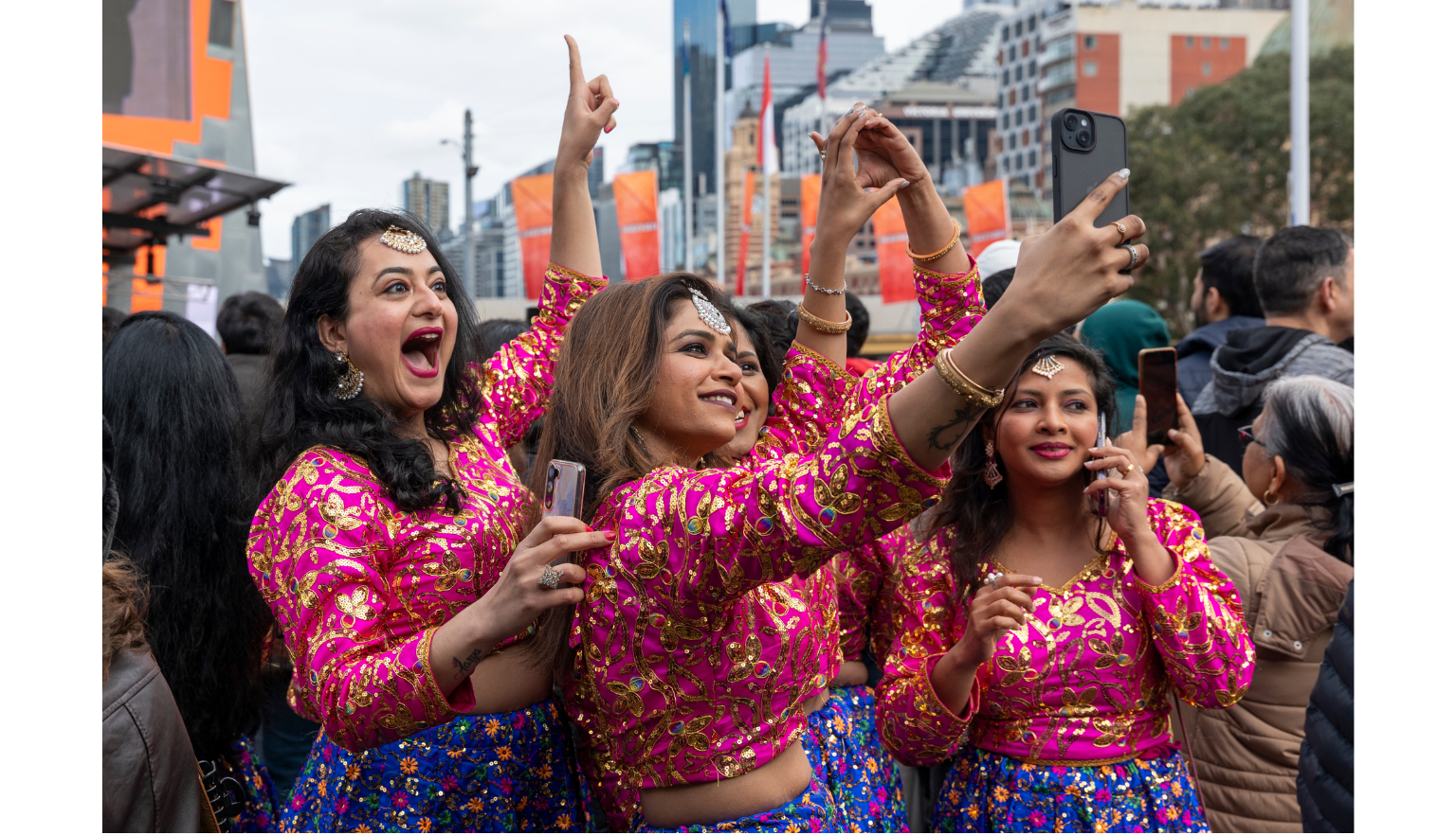 Women from the dance group Bollydance Dipti in pink costumes taking a selfie in a crowd