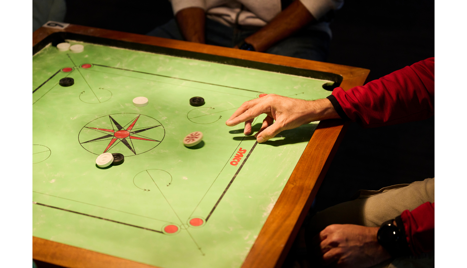 Green carrom board with a player picking up a piece