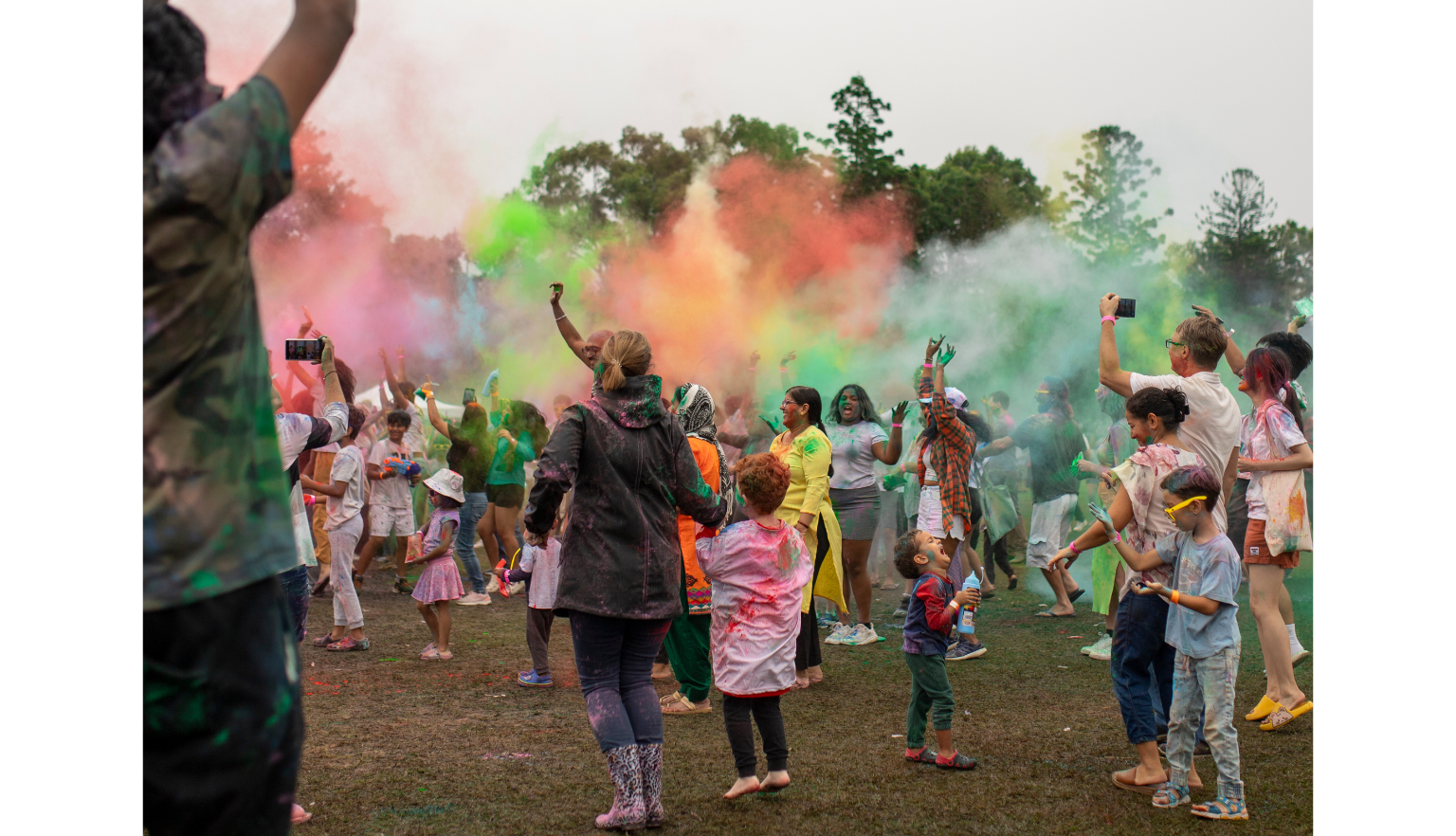 Adults and children in a park throwing gulal, colourful powders, in the air