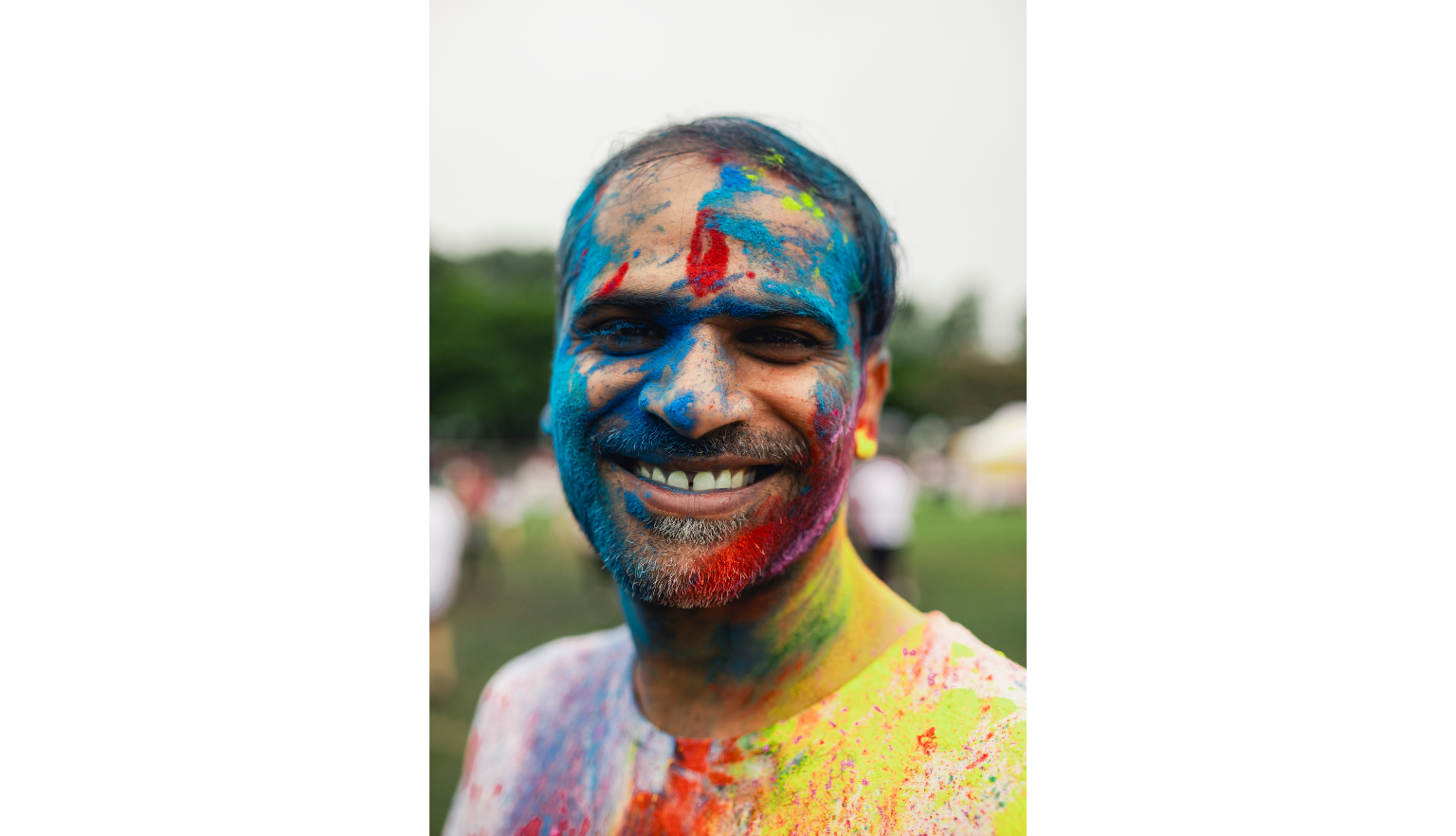 Man with multicoloured powder, gulal, on his face smiling at the camera