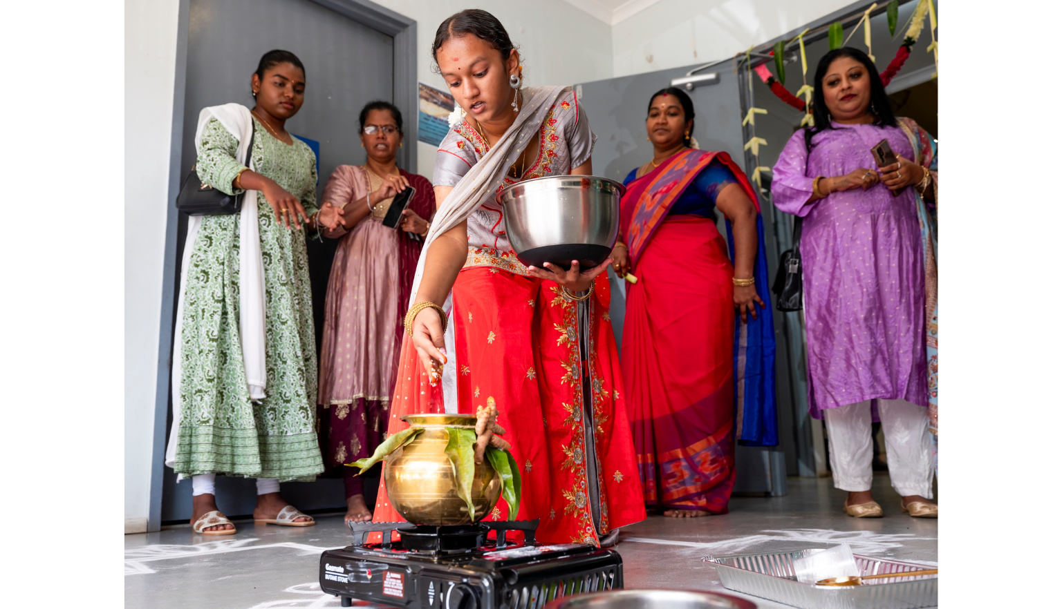 Woman in traditional dress throwing rice into a pot, with four women standing behind her