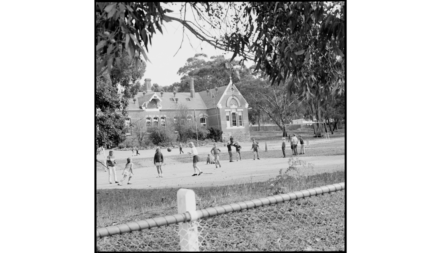 A black and white photograph of children playing in a schoolyard in Victoria