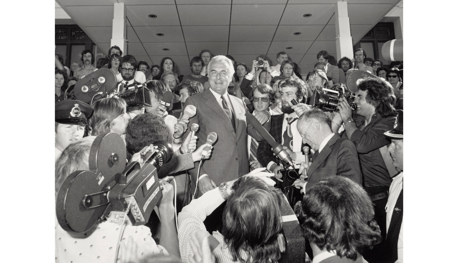 Black and white photo of Gough Whitlam speaking at Parliament House surrounded by reporters