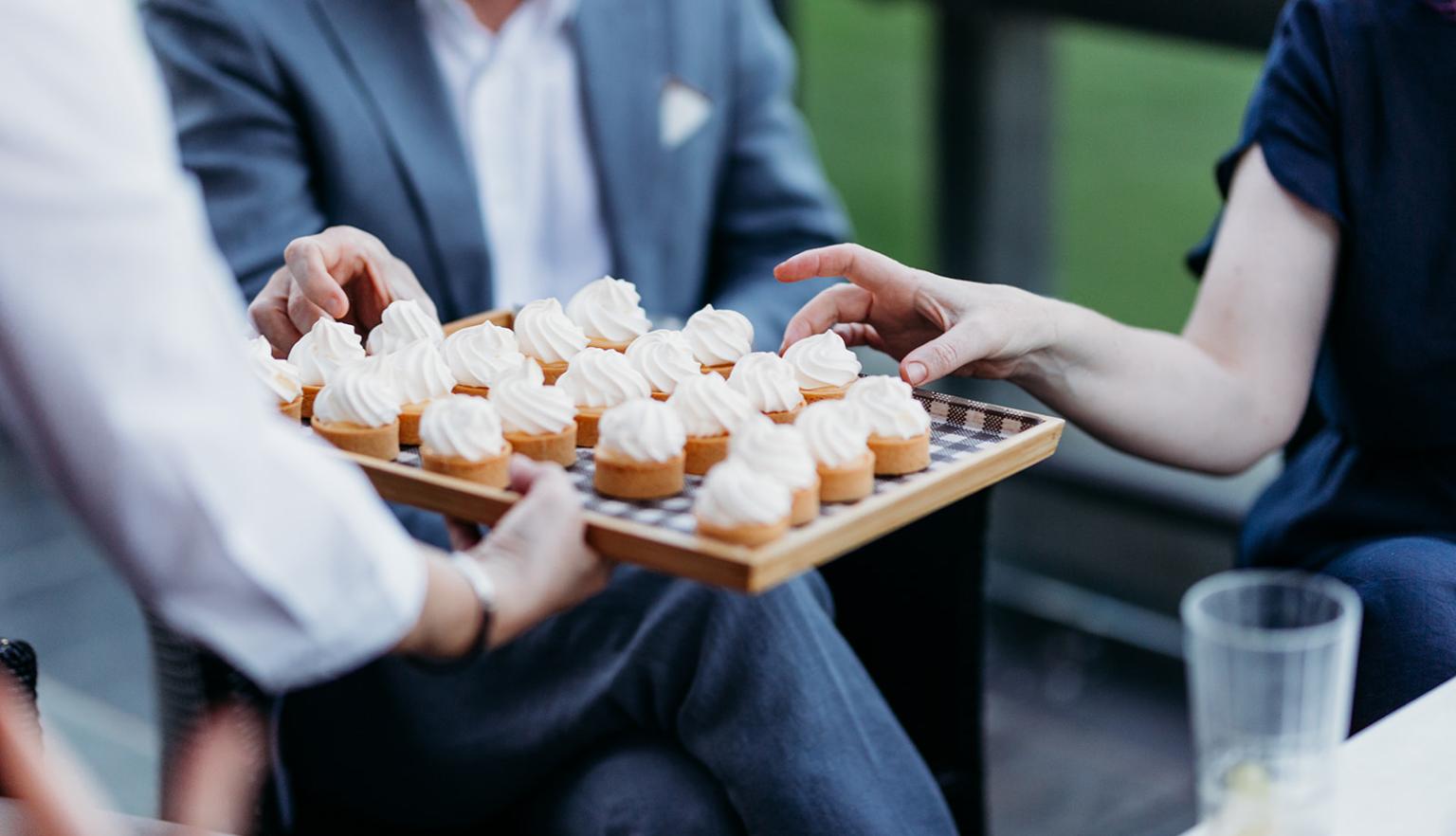People reaching for small deserts being held out to them on a tray