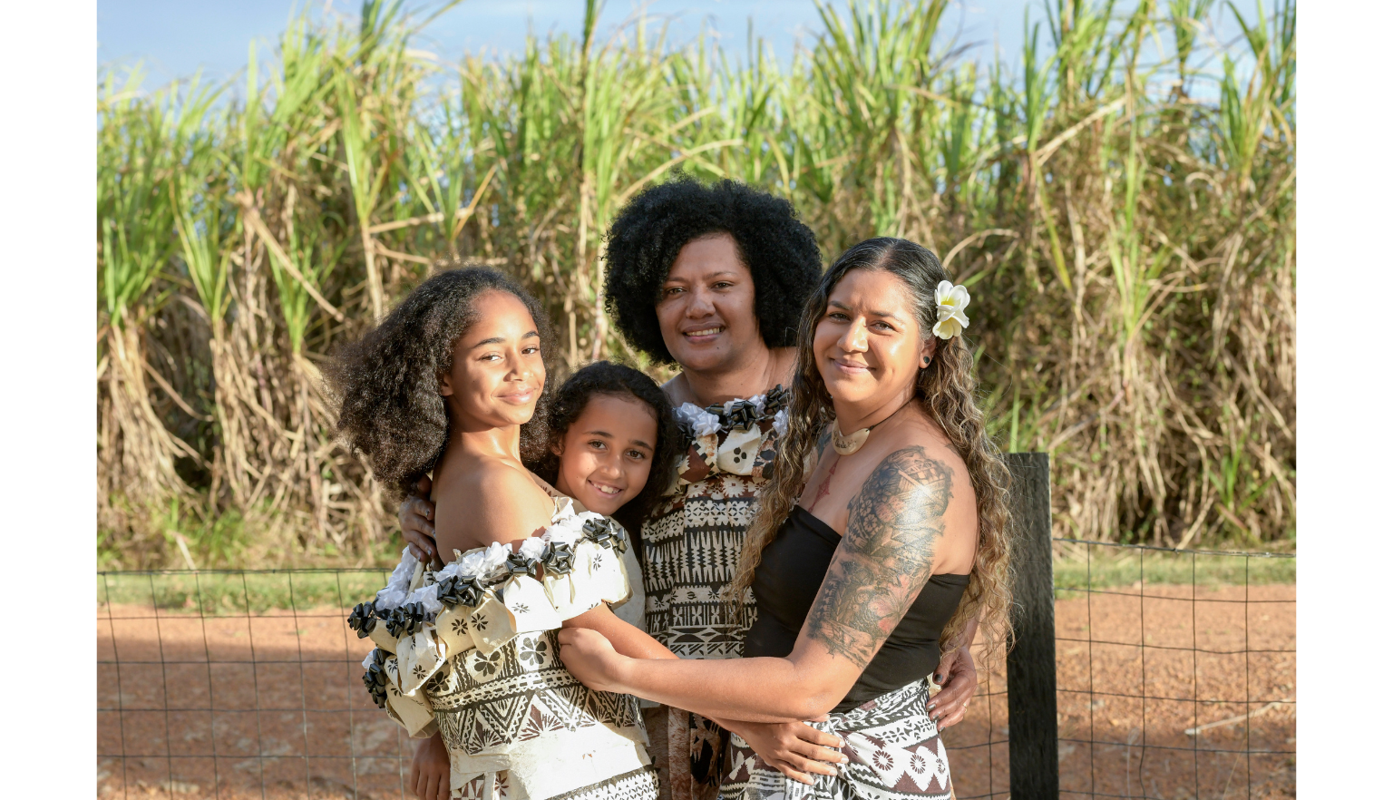 Four Fijian women of various ages wearing dresses smiling and embracing