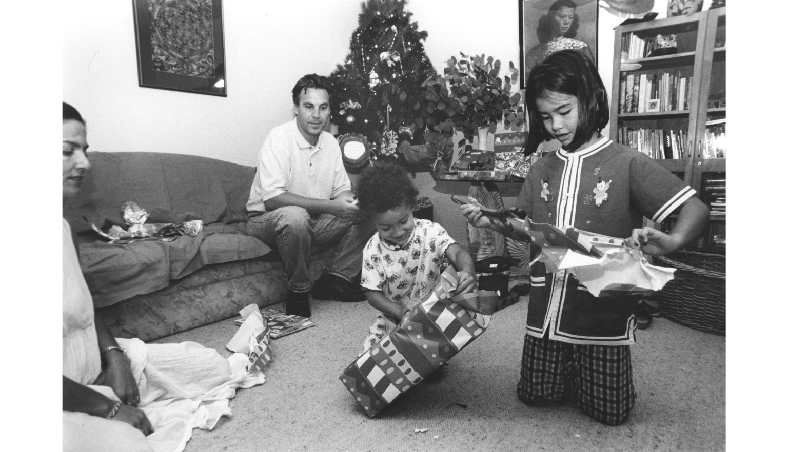 Black and white photo of two children opening Christmas presents, with two adults watching on