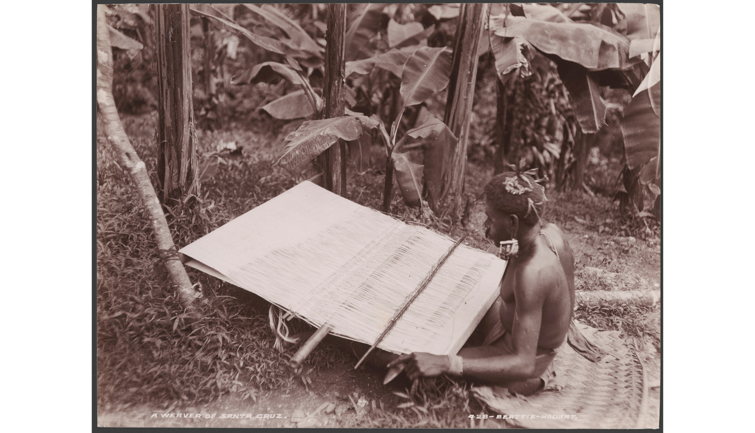 Man sitting on the ground weaving with a large loom
