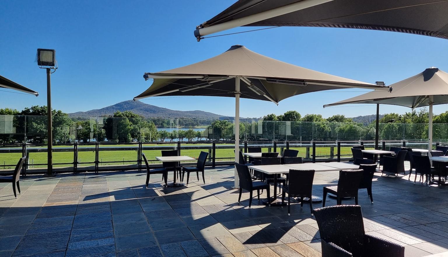 Outdoor seating area of Bookplate cafe with tables covered by umbrellas looking out at Lake Burley Griffin on a sunny cloudless day
