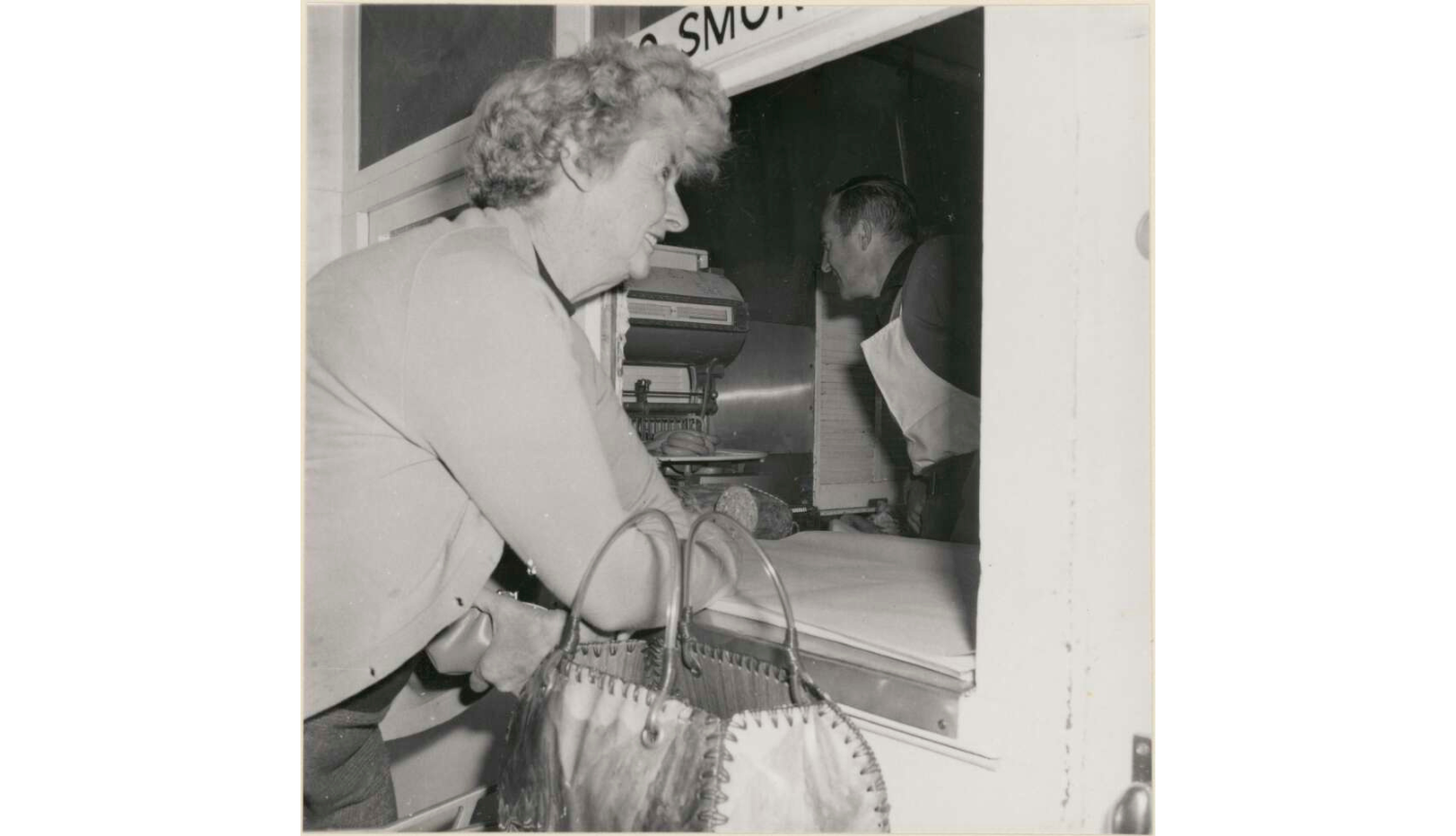 Black and white photo of a woman leaning on the window to the butcher on the Tea and Sugar train on the Trans Australia Railway