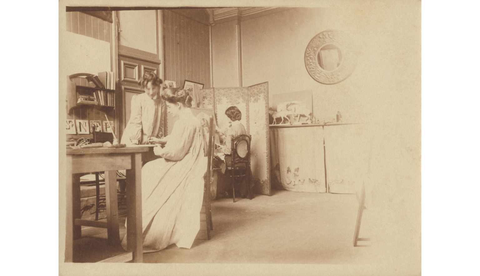Sepia-toned photo of Eirene Mort sitting at a table in her art studio