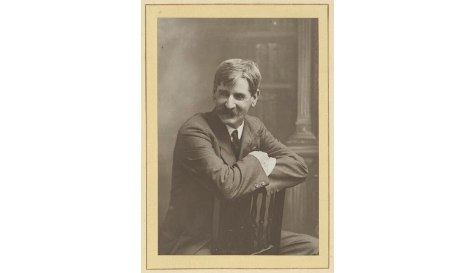 Black and white picture of Henry Lawson seated reverse on a chair, looking to the left off camera