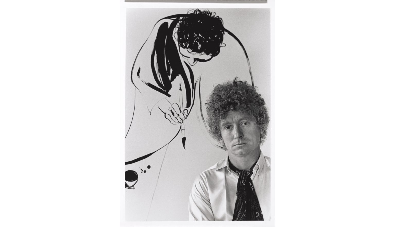 Black and white portrait of Brett Whiteley in front of a piece of calligraphy-styled art.