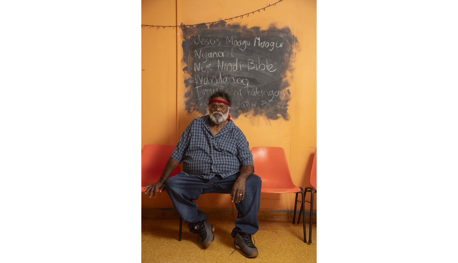 Pastor Geoffrey Stokes, seated on a red chair in front of an orange wall