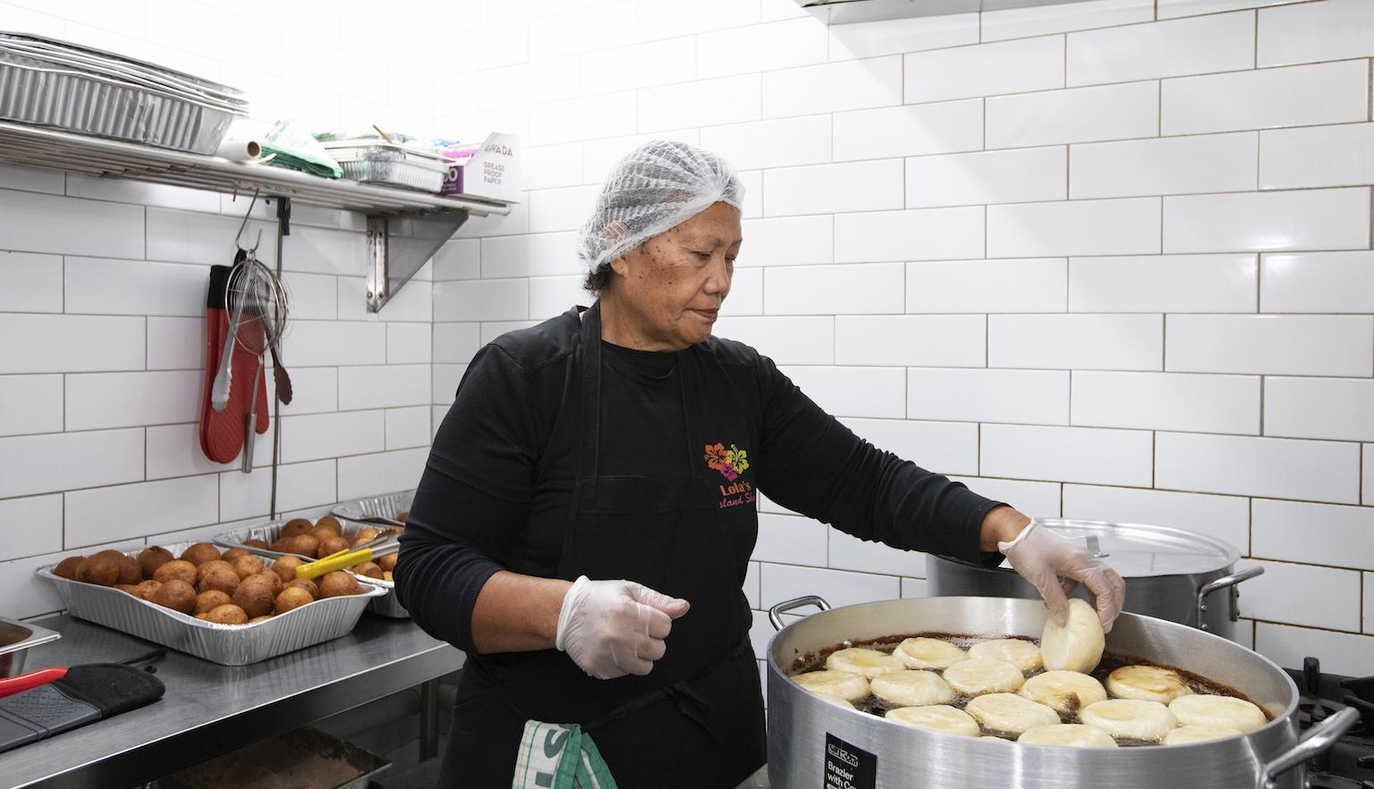 Woman in a hairnet placing pork buns in a large pot of oil