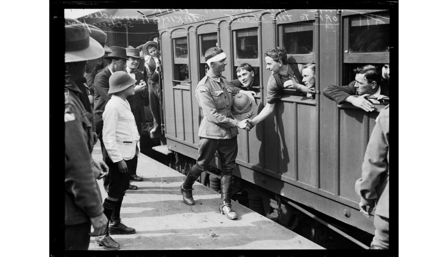 A black and white photograph capturing a group of young men gathered around a train car, with one man in a uniform interacting with another.