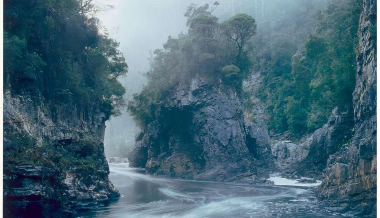 Misty river flowing through a deep, rugged gorge with steep, moss-covered cliffs on both sides.