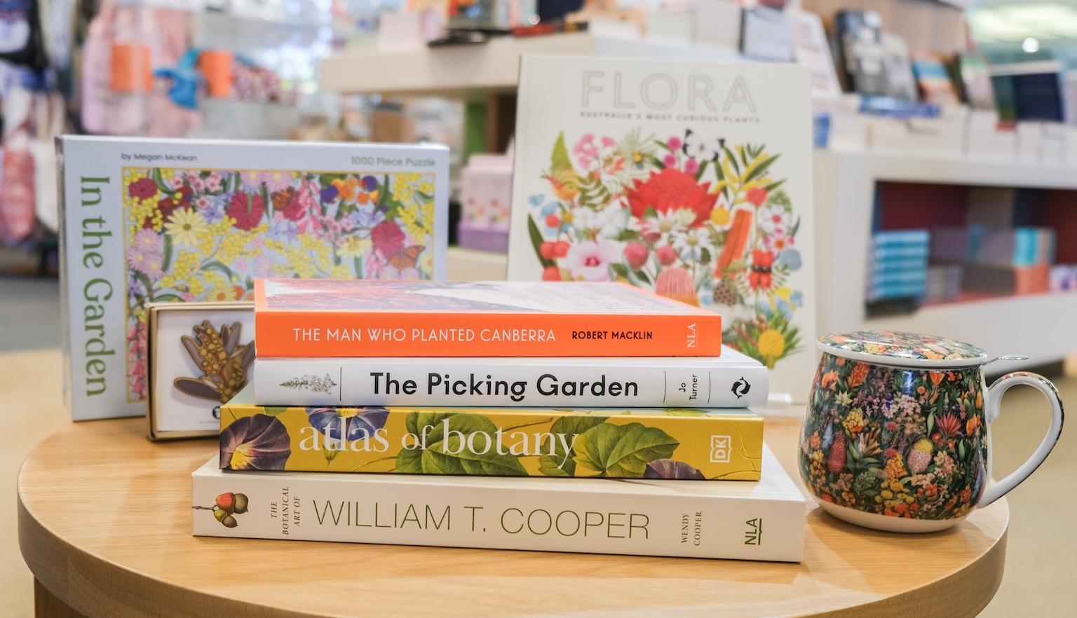 A table in the Bookshop with books, a mug, a puzzle and a wooden wattle brooch.