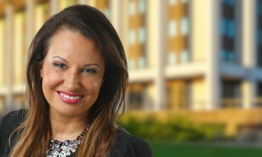 Eualayai/Gamillaroi woman with long brown hair wearing a black top and statement necklace smiling and standing in front of the National Library building