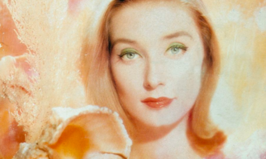 Artistic image of a blonde woman with light eyes smiling slightly in front of a pink and orange background