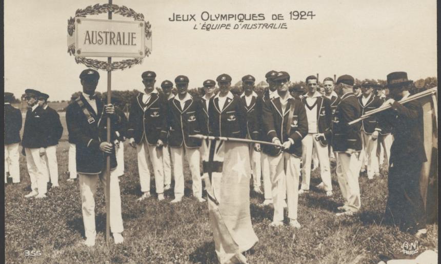 Group of men in white pants and dark blazers standing in a field. One of them holds a previous version of the Australian flag and another a sign that Reads 'Australie'