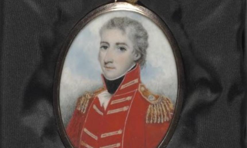 A painted locket portrait of a man in a red military uniform. The locket is resting on some black material.