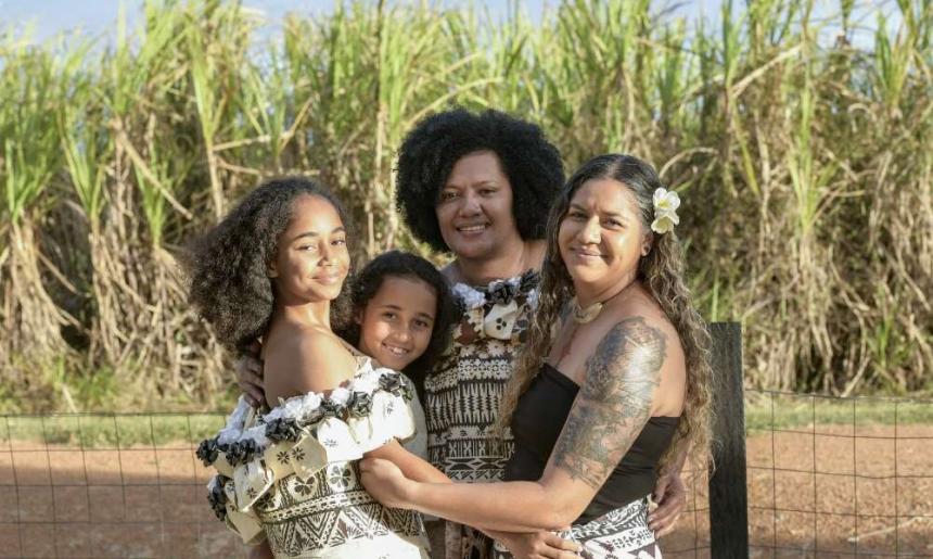 Four Fijian women of various ages wearing dresses smiling and embracing