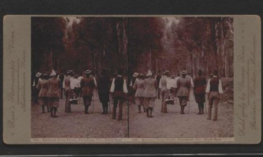 An old photograph of people in sensible clothing going for a walk in the bush.